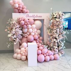 the balloon arch is decorated with pink and white balloons, flowers and trees in front of it