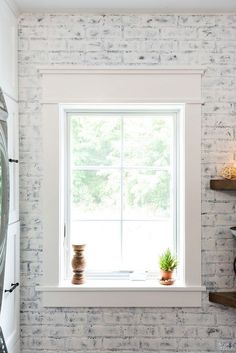 a white brick wall with a window and potted plants on the ledge in front of it