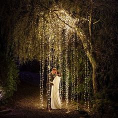 a bride and groom standing under an archway covered in fairy lights