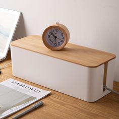 an alarm clock sitting on top of a white box next to a laptop and pen