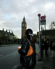 a woman standing on the side of a road next to a street sign with a clock tower in the background