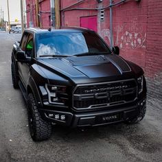 a black truck parked in front of a red brick building with graffiti on the walls