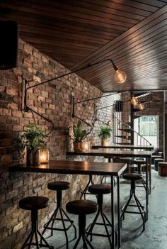 a brick wall with several stools and tables in front of it, along with lights hanging from the ceiling