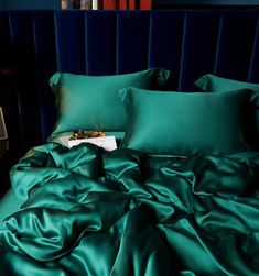 a bed with green sheets and pillows in a dark blue room next to a window