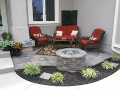 a patio with chairs, fire pit and plants on the side of the house in front of it