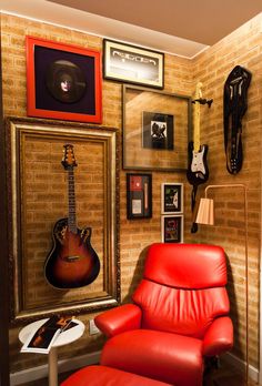 a red leather chair sitting in front of a wall with pictures and guitars on it