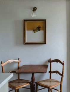 two wooden chairs sitting at a small table in front of a framed picture on the wall