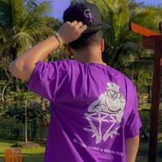 a man wearing a purple shirt and black hat standing in front of a wooden cross