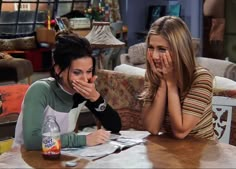 two young women sitting at a table with drinks and papers in front of their faces