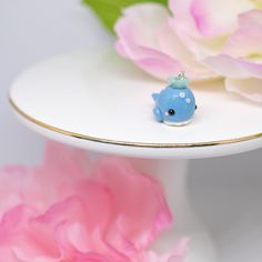 a small blue bird figurine sitting on top of a white plate next to pink flowers