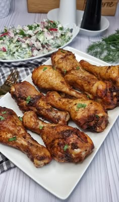 some chicken wings are on a white plate next to a salad and a silver fork