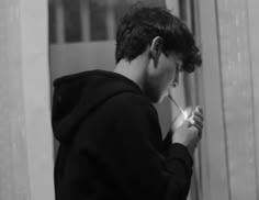 a young man is brushing his teeth in front of the mirror while wearing a hoodie