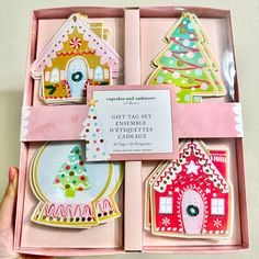 an open pink box filled with assorted cut out gingerbread houses and christmas trees