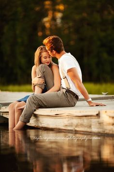 a man and woman sitting on a dock next to each other looking at each other