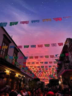 many people are walking down the street with flags flying in the air above them at night