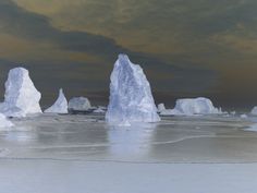 icebergs are standing in the middle of an icy lake under a cloudy sky