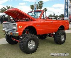 an orange pickup truck with its hood open on display at a car and truck show