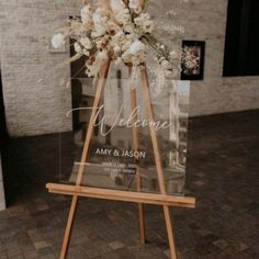 a clear acrylic sign that says welcome with flowers in it on a wooden easel