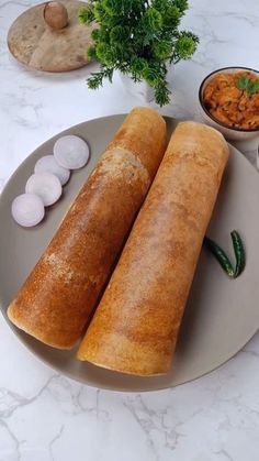 two large rolls on a plate next to small bowls of vegetables and other food items