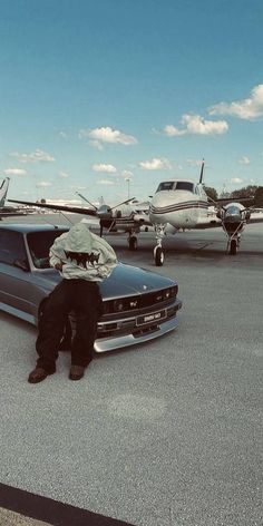 a man sitting on the hood of a car in front of an airplane