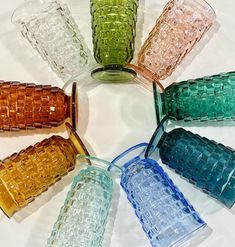 there are many different colored glass cups in the middle of a circular arrangement on top of each other