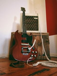 a red electric guitar sitting on top of a wooden floor next to an old telephone