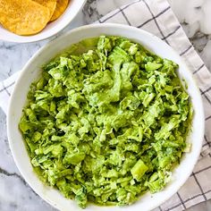 a bowl filled with guacamole next to tortilla chips on a table