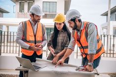 three people in hard hats looking at something on top of a table with a laptop