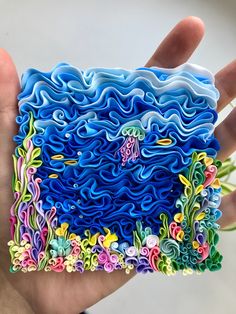 a hand holding a piece of art made out of paper and colored flowers on it