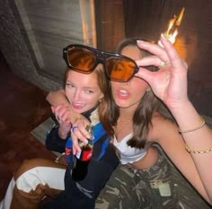 two young women sitting next to each other holding up their hands with fire in the background