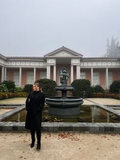 a woman standing in front of a fountain with a building in the back ground behind her