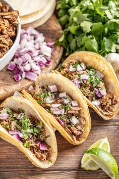 three tacos with shredded meat, onions and cilantro on a cutting board