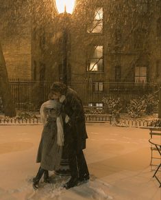 a man and woman standing in the snow near a building with a street light behind them