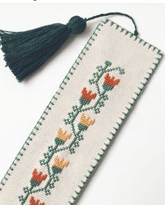 a cross stitch bookmark with flowers and tassels on the front, along with a tassel