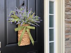 a black door with a green bow and purple flowers in a basket hanging on it