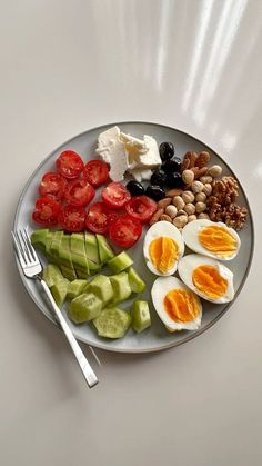 an egg, tomatoes, cucumber, olives, and beans on a plate