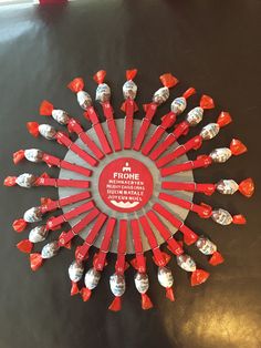 a red and white clock with lots of small objects on it's face in the shape of a sunburst