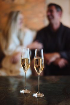 two glasses of champagne sitting on top of a table next to a man and woman