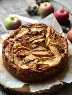 an apple pie sitting on top of a piece of wax paper next to some apples