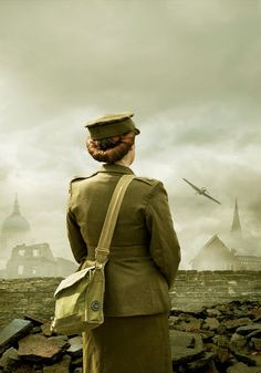 a woman in an army uniform standing on rocks looking at planes flying over the city