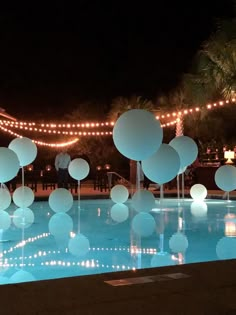 white balloons floating in the air over a pool at night with string lights strung around it