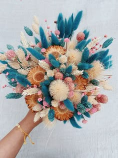 a hand holding a bouquet with feathers and flowers