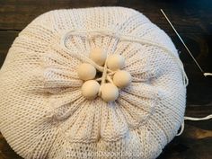 a white knitted pillow with four eggs on it and some knitting needles in the background