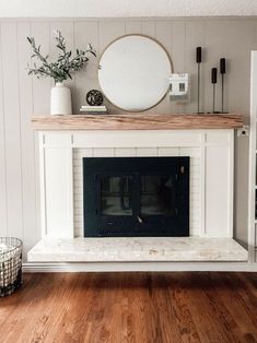 a living room with a white fireplace and wood flooring on the wooden floors, along with a round mirror above it