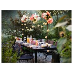 an outdoor dining table with flowers and drinks on it in the middle of a garden