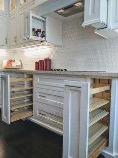 a kitchen with white cabinets and wooden drawers on the bottom shelf is filled with spices