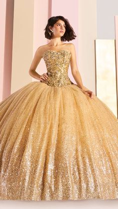 a woman in a gold ball gown standing next to a pink wall with her hands on her hips