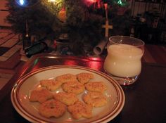 a plate of cookies next to a glass of milk on a table with a christmas tree in the background