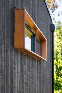 an open window on the side of a wooden building with trees in the back ground