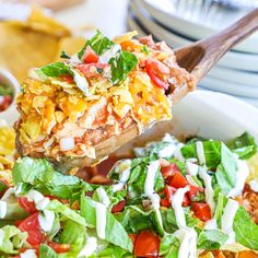 a wooden spoon full of mexican food with lettuce, tomatoes and cheese on top